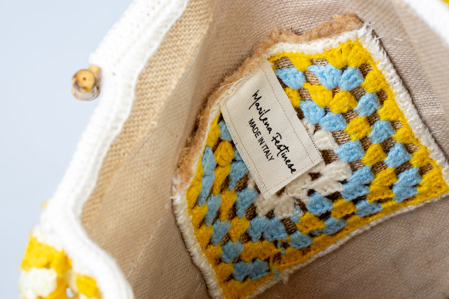 Shopping bag dal design patchwork. Un pezzo di pregevole fattura composto da tre tele che avvolgono la borsa nella sua interezza. Questa bag echeggia la tradizione riportando in auge gli antichi pizzi di un tempo. I manici in bambù, uno dei simboli identificativi del brand, permettono di indossarla come borsa a mano. Di manifattura artigianale, prodotta in Italia.