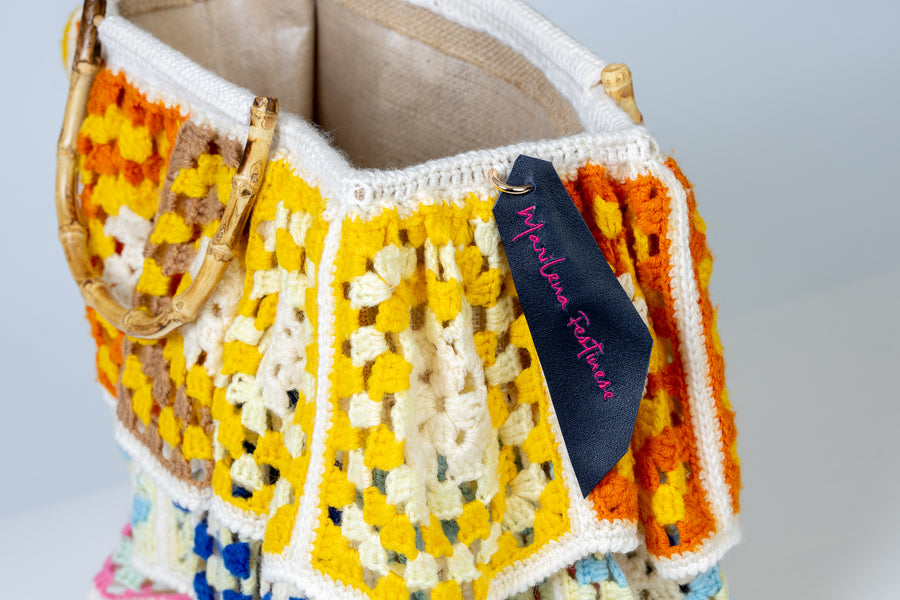 Shopping bag dal design patchwork. Un pezzo di pregevole fattura composto da tre tele che avvolgono la borsa nella sua interezza. Questa bag echeggia la tradizione riportando in auge gli antichi pizzi di un tempo. I manici in bambù, uno dei simboli identificativi del brand, permettono di indossarla come borsa a mano. Di manifattura artigianale, prodotta in Italia.
