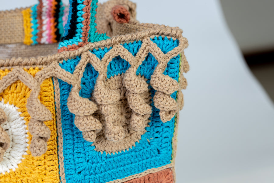 Design patchwork coronato da una splendida e sottile cornice beige, completata da un manico multicolore e dagli “sbaruffi” elicoidali. Tote Bag eccentrica e vivace, realizzata all’uncinetto. La sua tracolla rimovibile permette di portare la borsa a spalla. Di manifattura artigianale, prodotta in Italia.