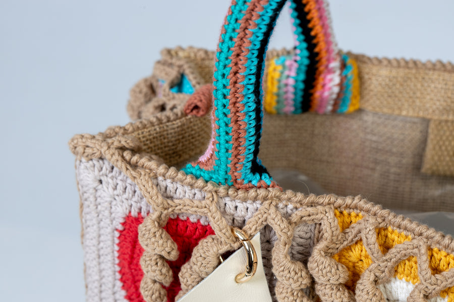 Design patchwork coronato da una splendida e sottile cornice beige, completata da un manico multicolore e dagli “sbaruffi” elicoidali. Tote Bag eccentrica e vivace, realizzata all’uncinetto. La sua tracolla rimovibile permette di portare la borsa a spalla. Di manifattura artigianale, prodotta in Italia.