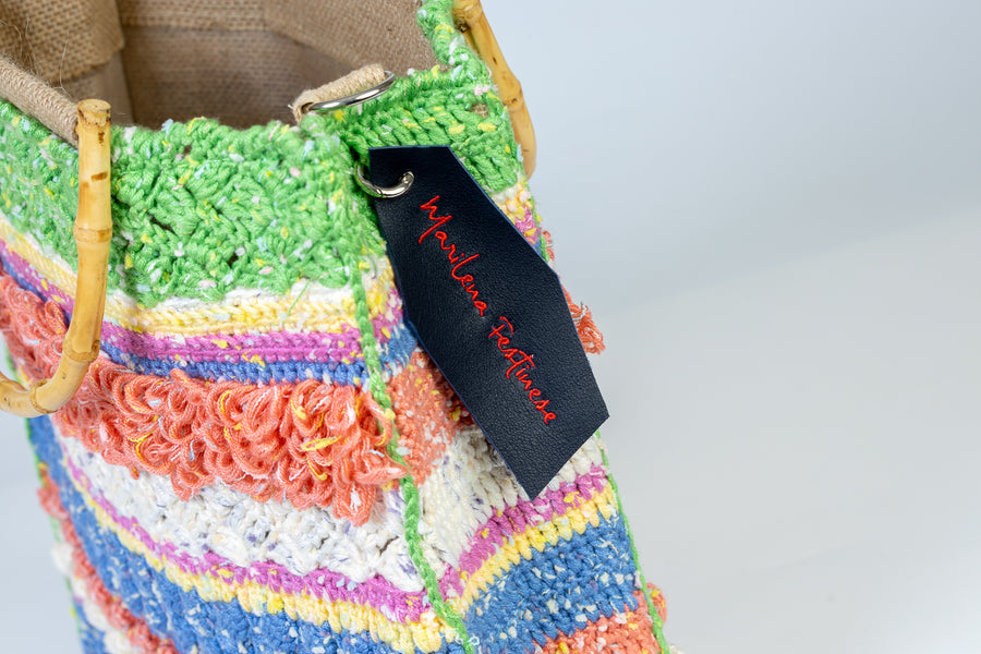 Una composizione di righe di filati diversi lavorati ad un uncinetto, regalano un lavoro unico pieno di allegria. I manici in bambù, uno dei simboli identificativi del brand, permettono di indossarla come borsa a mano; La sua tracolla rimovibile, invece, permette di portare la borsa a spalla. Di manifattura artigianal…