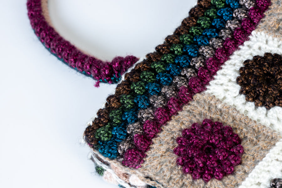 Sei linee all’uncinetto orizzontali dal verde al viola si uniscono per formare un angolo retto con quattro linee verticali dall’azzurro al rosa. I suoi lunghi manici morbidi realizzati mediante uncinetto, permettono di indossarla come borsa a mano. Di manifattura artigianale, prodotta in Italia.